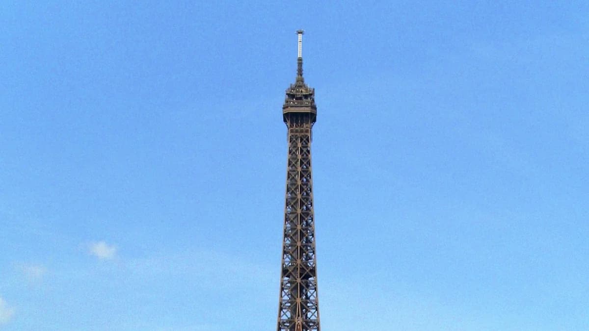 Photo by Waithamai, licensed under CC BY-SA 3.0 (Wikimedia Commons) The upper section of the Eiffel Tower in Paris, France, set against a clear blue sky