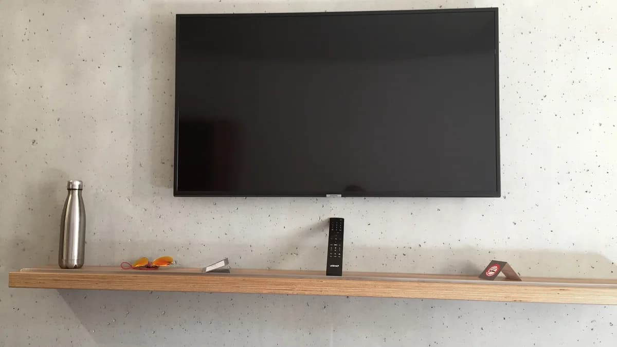 Photo by Air fans, licensed under CC BY-SA 4.0 (Wikimedia Commons) Wall-mounted Samsung television with its screen off and a remote control resting on a shelf below it